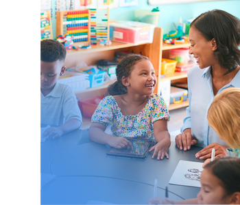 A teacher sitting at a table with a group of students and smiling.