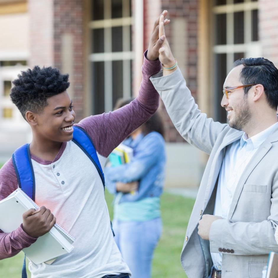 A student and a teacher high five outside of the high school. 