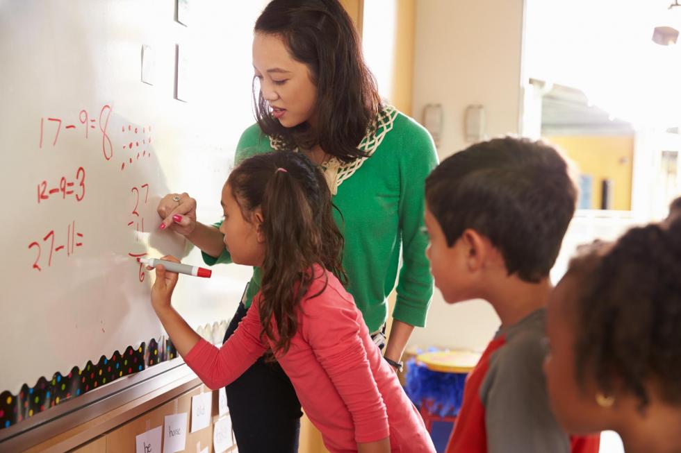 Teacher and elementary school students solve math problems at a whiteboard