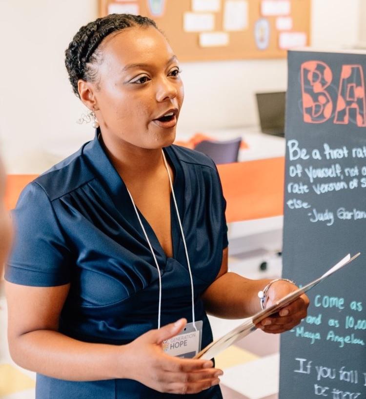 Nija Simmons, an African American college student parent stands holding a paper and presents to her class