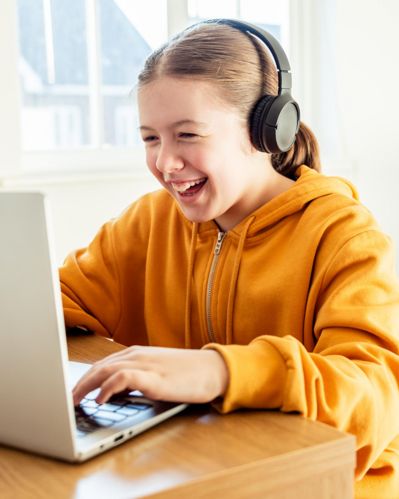 Middle school girl with headphones smiling at a computer screen