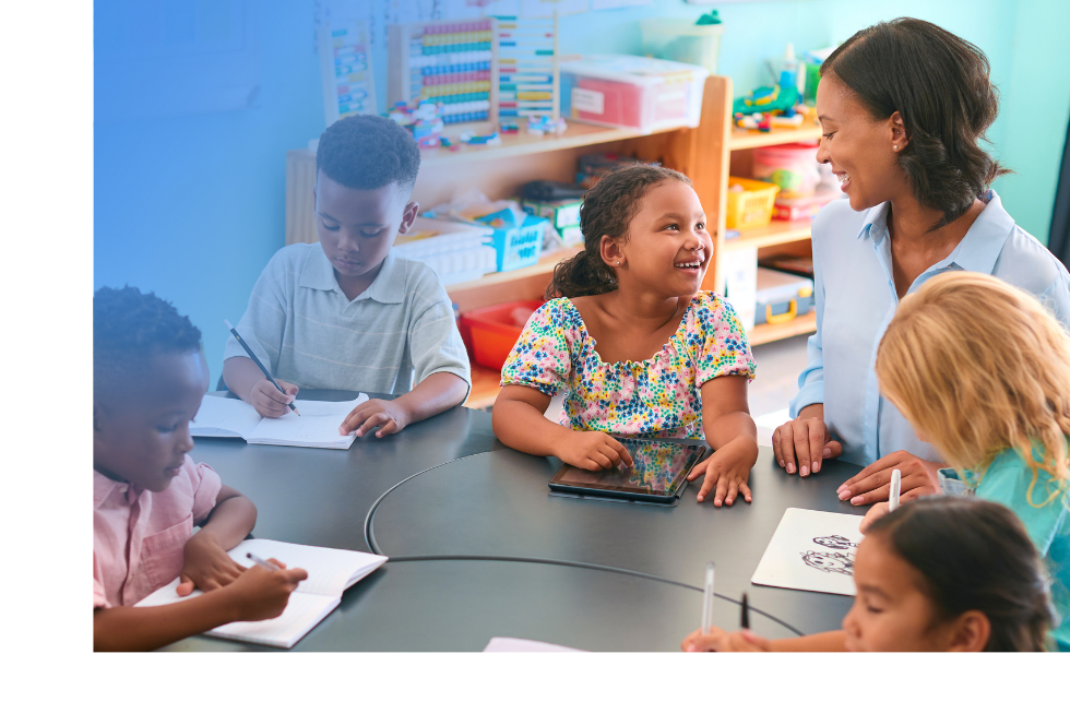 A teacher sitting at a table and working with 5 young students.