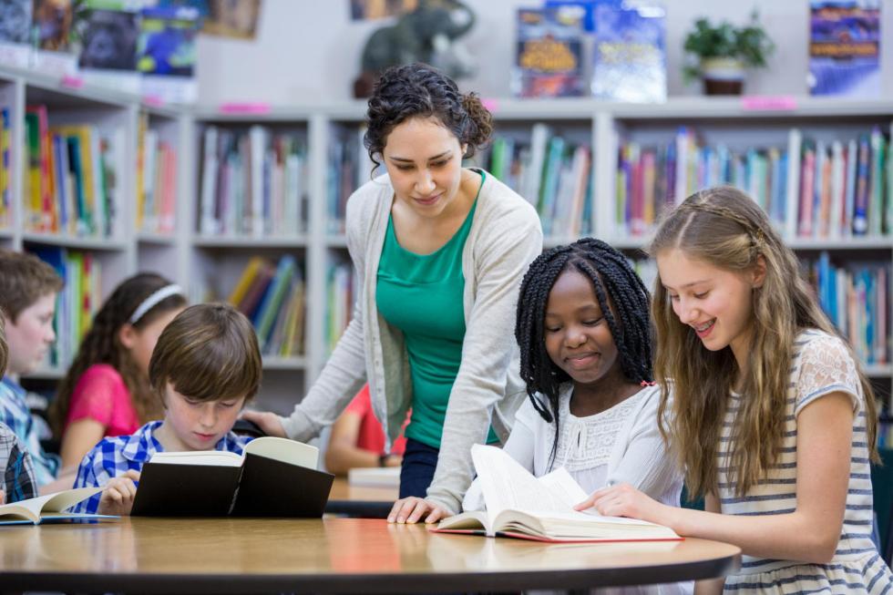 teacher overseeing student work in library 