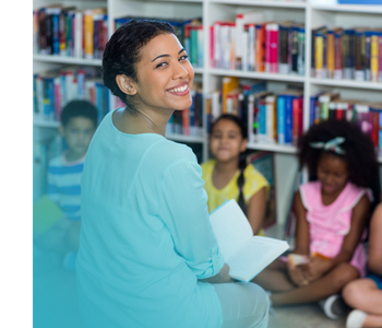 A teacher reading with a group of students in front of some bookshelves.