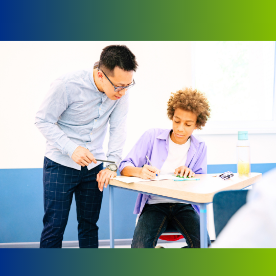 A teacher works with a student at his desk